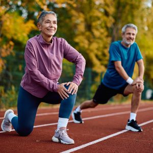 Zwei Senioren in Jogging-Outfits dehnen sich auf der Laufstrecke