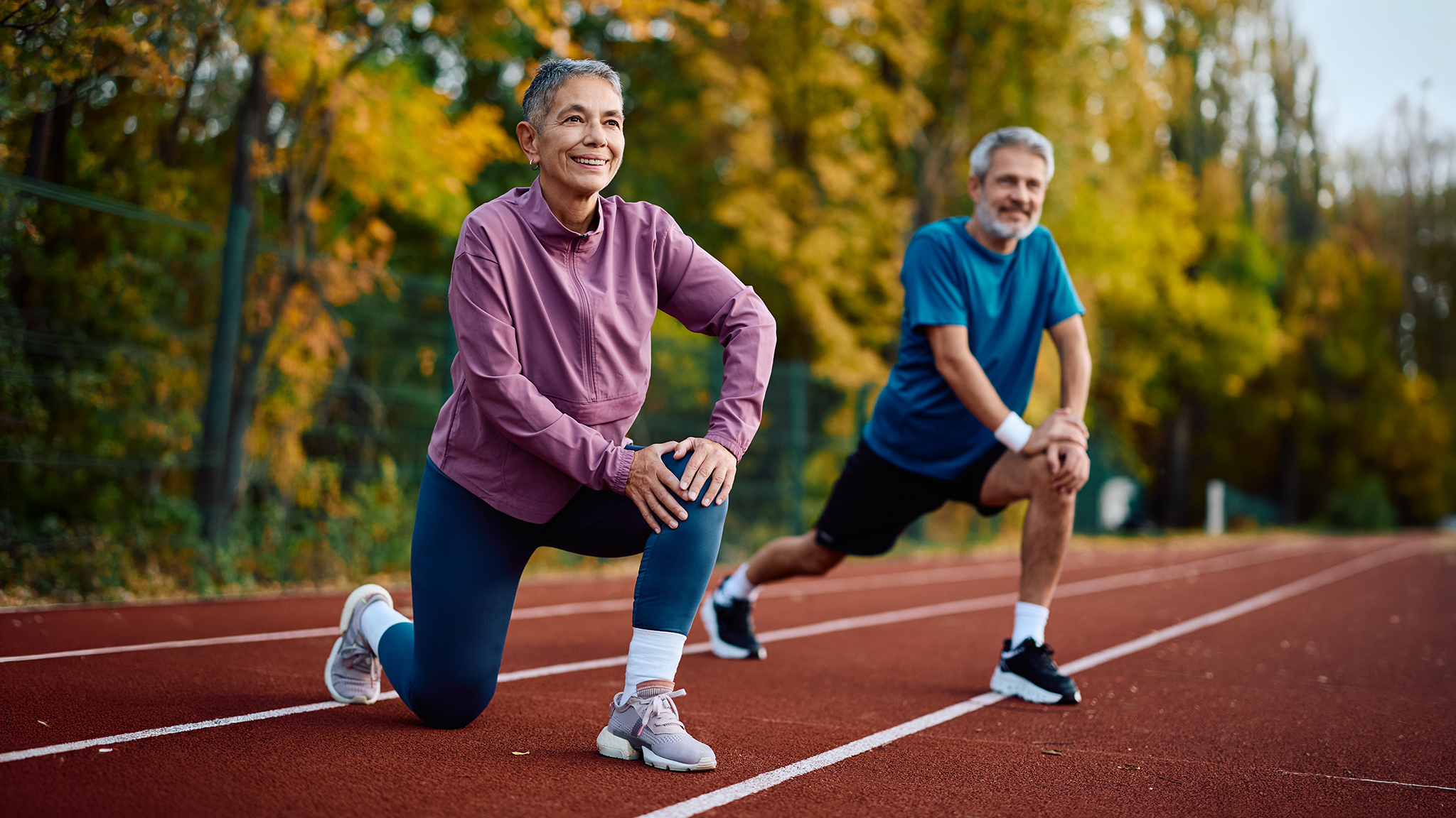 Zwei Senioren in Jogging-Outfits dehnen sich auf der Laufstrecke