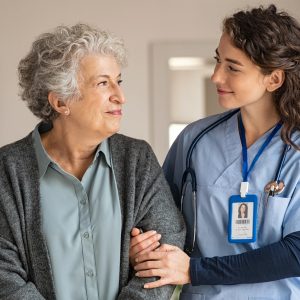 Lächelnde Pflergin, die lächelnde Seniorin stützt