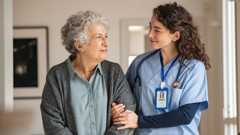 Lächelnde Pflergin, die lächelnde Seniorin stützt